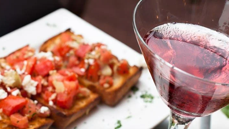 A glass of red wine beside a plate of gourmet food on a wooden table.