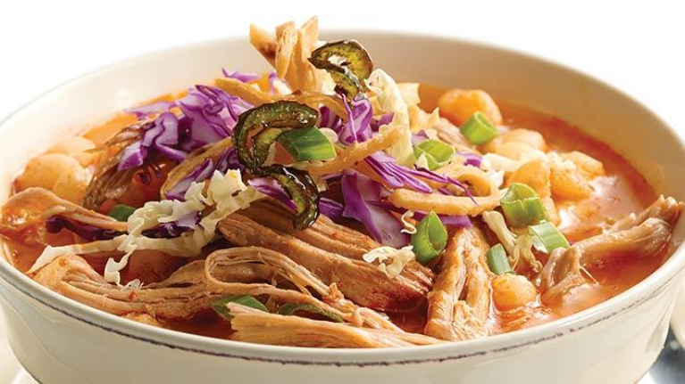 A bowl of chili featuring shredded pork and a variety of colorful vegetables, garnished for a hearty meal.