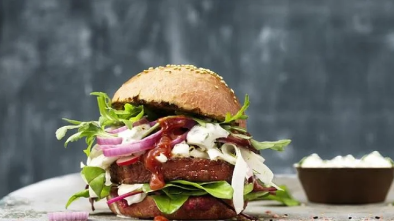 Two burgers on a table next to a bowl of sauce, ready to be enjoyed.