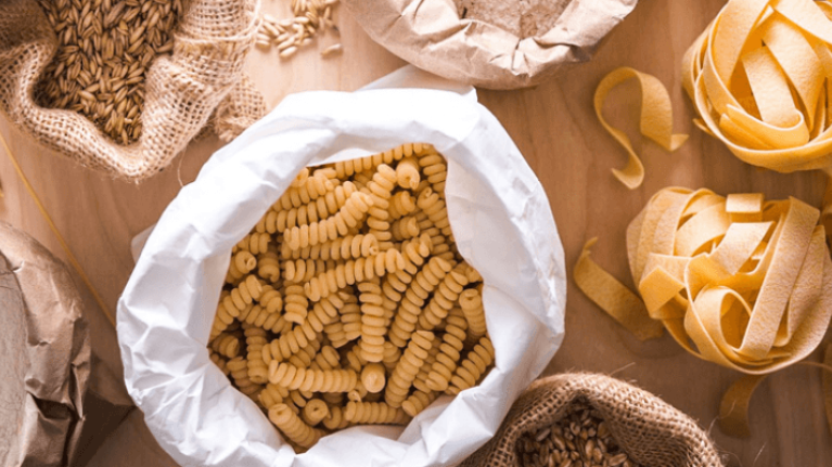 Different pasta shapes in burlap bags on a wooden surface, with potential allergens.