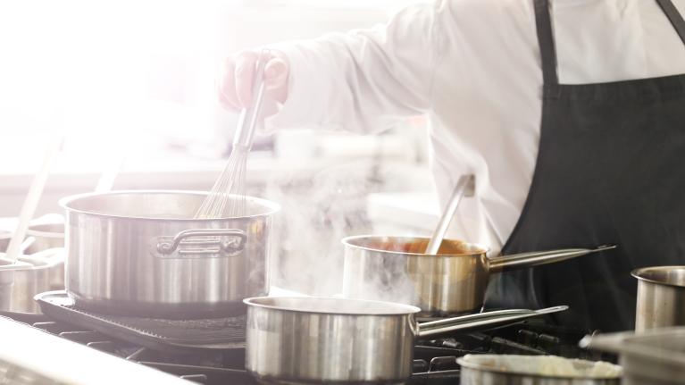 A man wearing a chef's apron is cooking in a modern kitchen, surrounded by utensils and fresh ingredients.