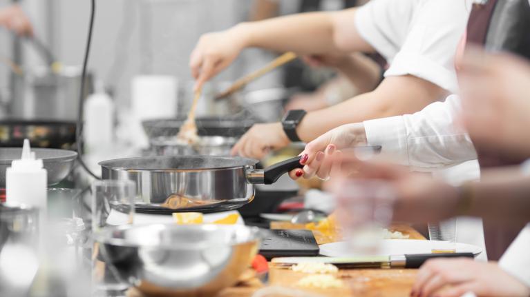 Group of people cooking together in a bright kitchen, preparing various dishes and enjoying the process.