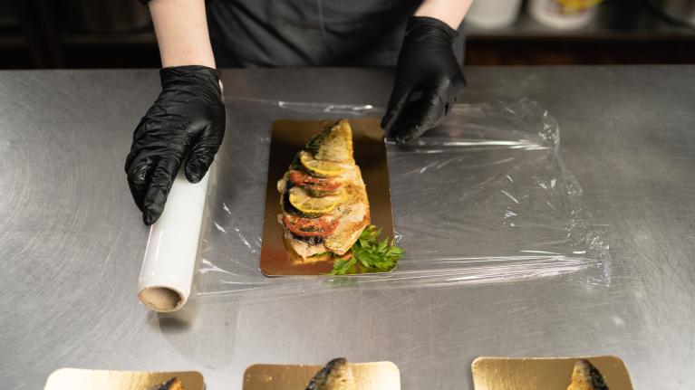 A person wearing black gloves carefully places fish onto a tray, preparing for presentation or cooking.