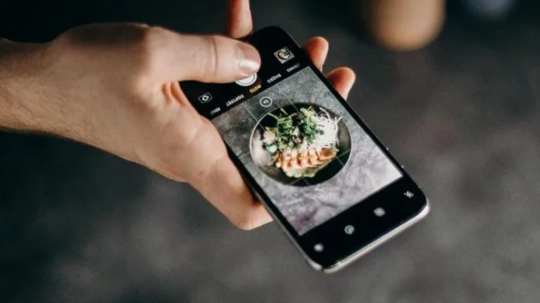A person is holding a smartphone displaying a colorful image of delicious food on the screen.