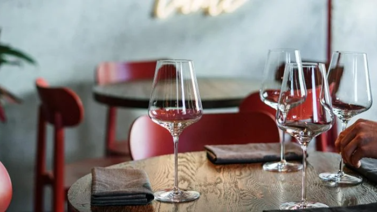 A man arranges a table, carefully placing wine glasses for an elegant setup.