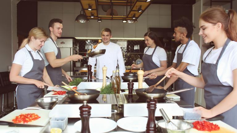 Chef cooking in a busy kitchen with others helping and preparing food together.