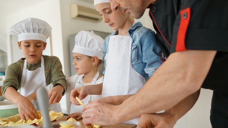 A group of children wearing chef hats happily preparing food together in a bright kitchen.