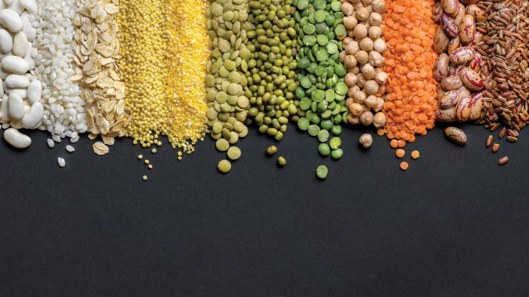 Varied grains, beans, and lentils arranged in colorful rows on a dark background.