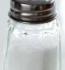A salt shaker filled with white salt, resting on a wooden table.