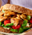A hand presenting a sandwich filled with chicken and spinach, featured in the Garden Gourmet Plant Proteins Recipes Booklet