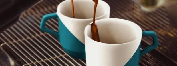 Two coffee cups are being poured into one another, showcasing an interaction of steaming coffee.