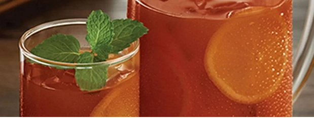 A clear pitcher filled with tea, topped with a slice of orange and sprigs of mint.