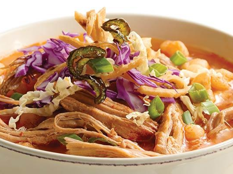 A bowl of chili featuring shredded pork and a variety of colorful vegetables, garnished for a hearty meal.