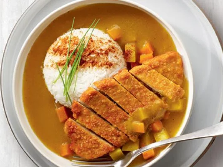 A bowl of curry served with rice and colorful vegetables, showcasing a vibrant and appetizing meal.