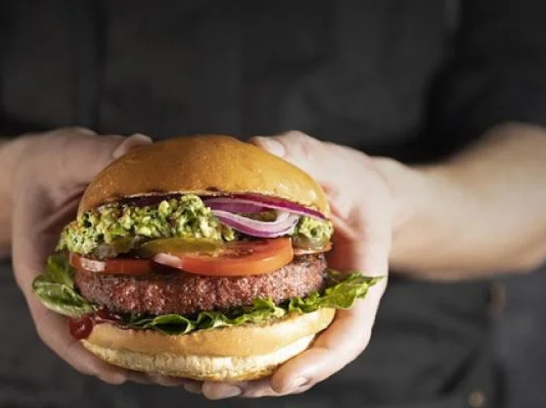 A person smiling while holding a delicious hamburger in both hands, ready to take a big bite.