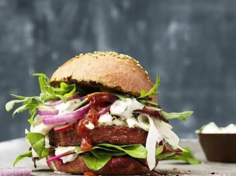 Two burgers on a table next to a bowl of sauce, ready to be enjoyed.