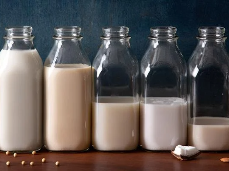 Variety of plant-based milks in glass bottles on a wooden table.