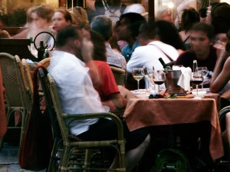 People enjoy meals at tables in a lively outdoor restaurant setting under clear skies.