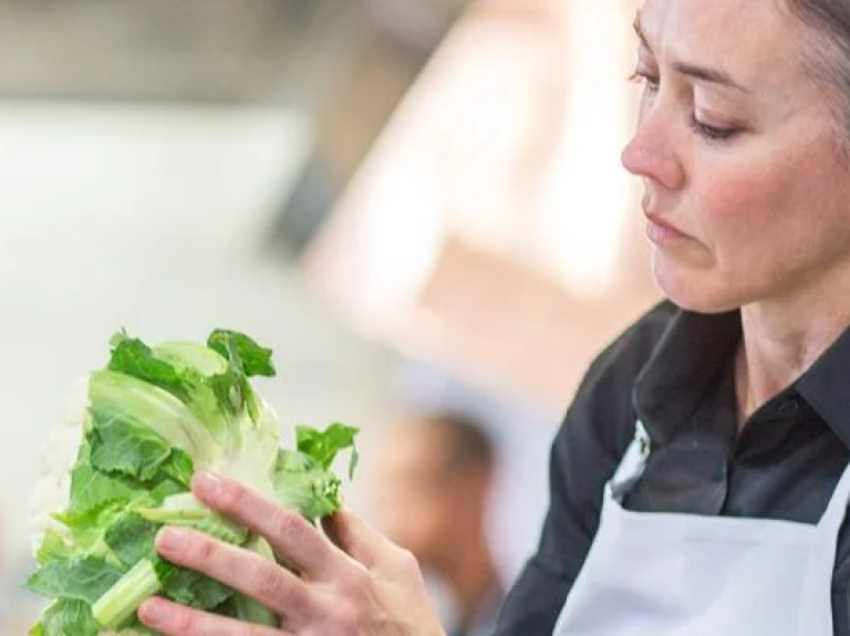 A woman stands in a kitchen, smiling as she holds a fresh salad in her hands.