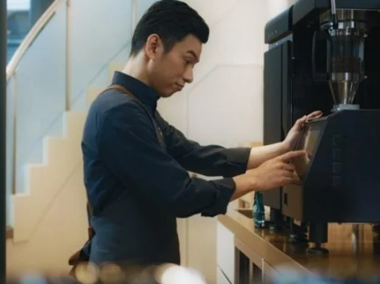 A man operates a machine in a factory, focused on his work amidst industrial equipment.