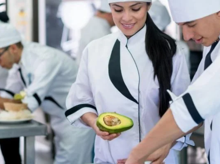 Chefs preparing dishes in a commercial kitchen filled with equipment and fresh ingredients.