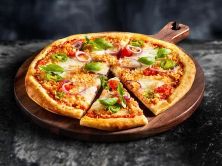 A pizza topped with cheese, fresh tomatoes, and basil, presented on a rustic wooden board.