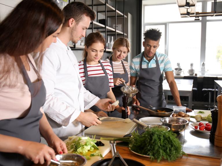 A diverse group of individuals collaborates in a kitchen, skillfully preparing various dishes together.