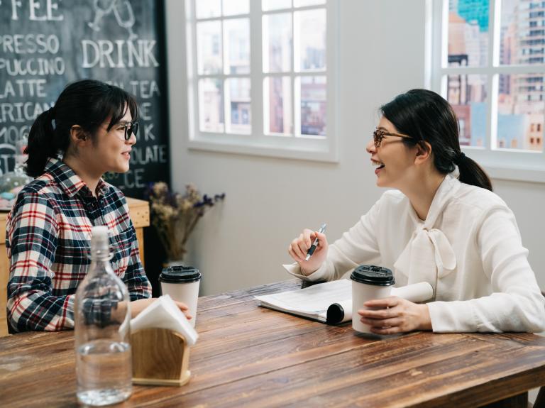 Two women engaged in conversation while sitting at a table, sharing smiles and ideas.
