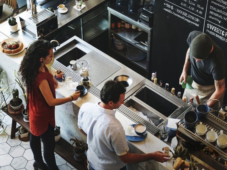 People ordering coffee at a busy café counter with barista preparing drinks.