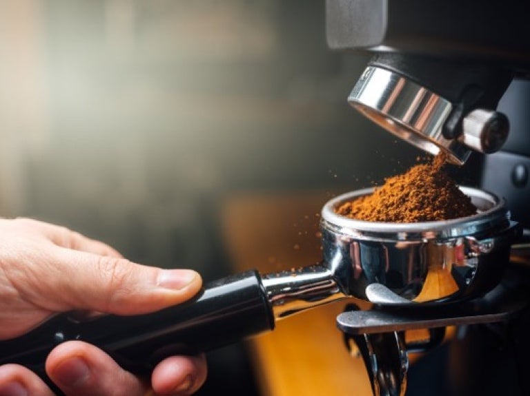 A person grinding coffee beans using an espresso machine in a bright kitchen setting.
