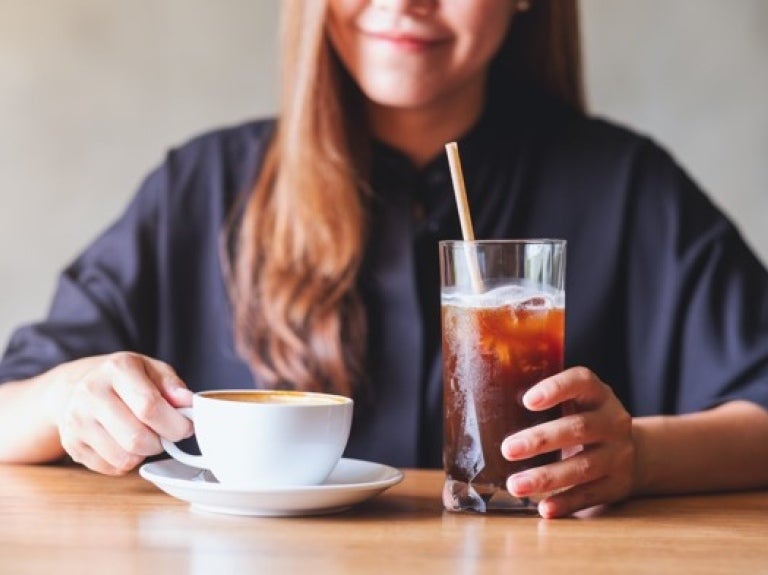 A woman with a cup of coffee and a straw, looking content while sipping her beverage.