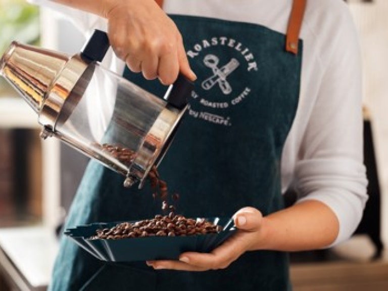 A woman in an apron pours coffee from a pot into a bowl, focusing intently on her task.