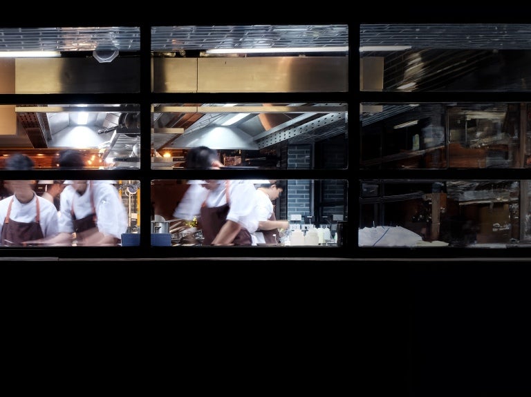 Busy restaurant kitchen seen through window with chefs preparing food in motion blur.