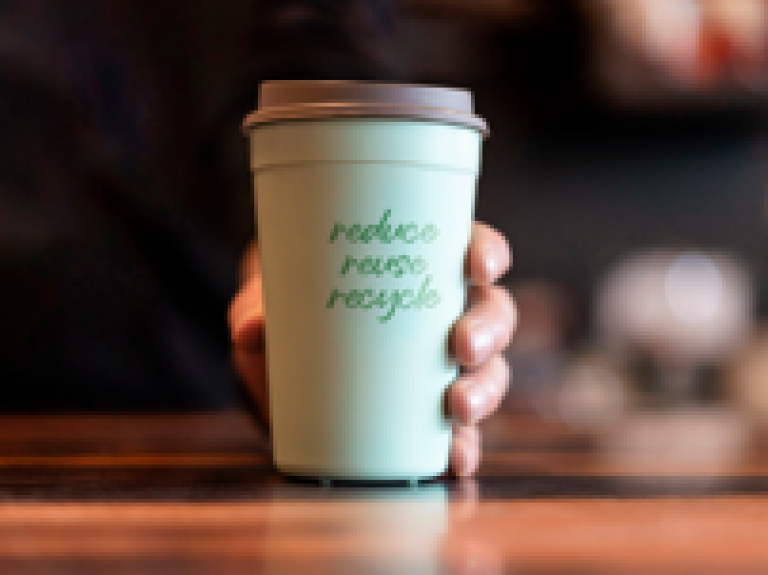 A person holds a green cup, promoting the message of reduce, reuse, recycle.