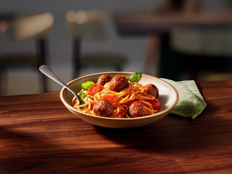A serving of spaghetti with meatballs and diced tomatoes in a white bowl, showcasing a hearty Italian dish.