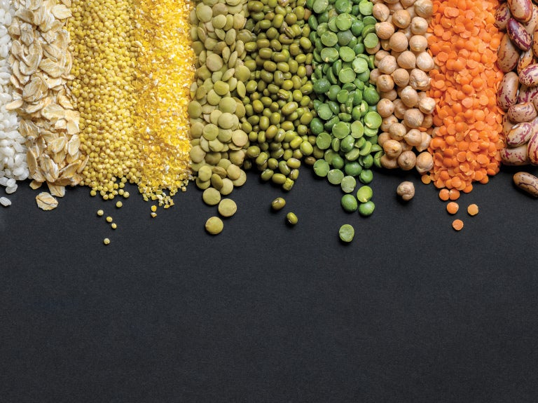 Varied grains, beans, and lentils arranged in colorful rows on a dark background.