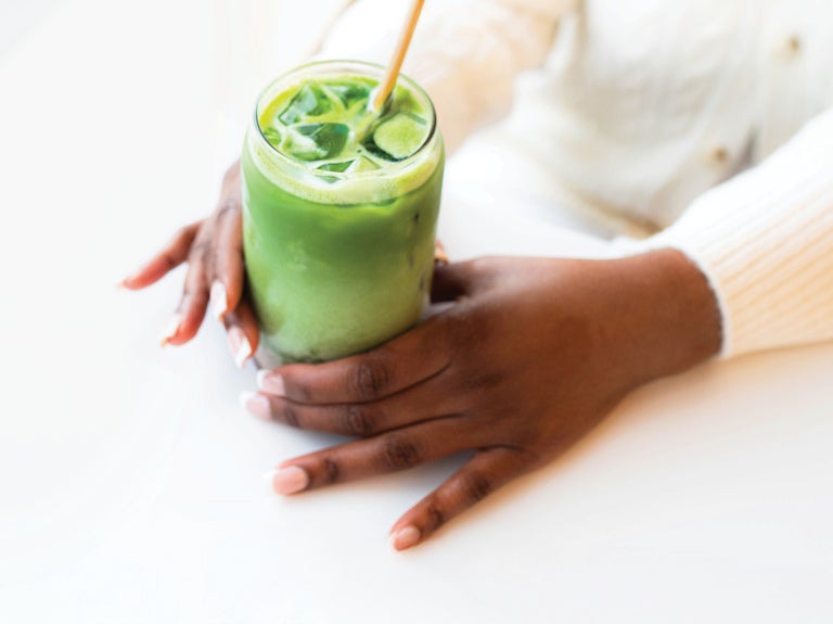 Hands holding a matcha drink with a straw on a white table.