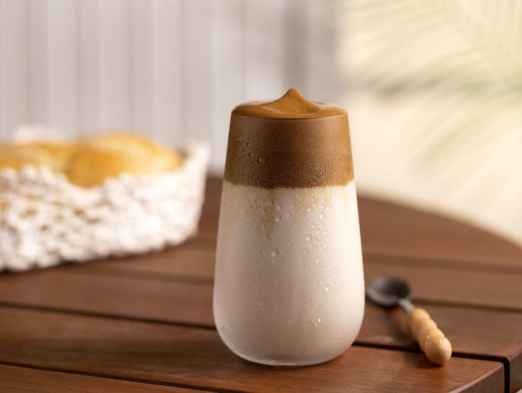 A glass of milk topped with a layer of brown foam or cream.