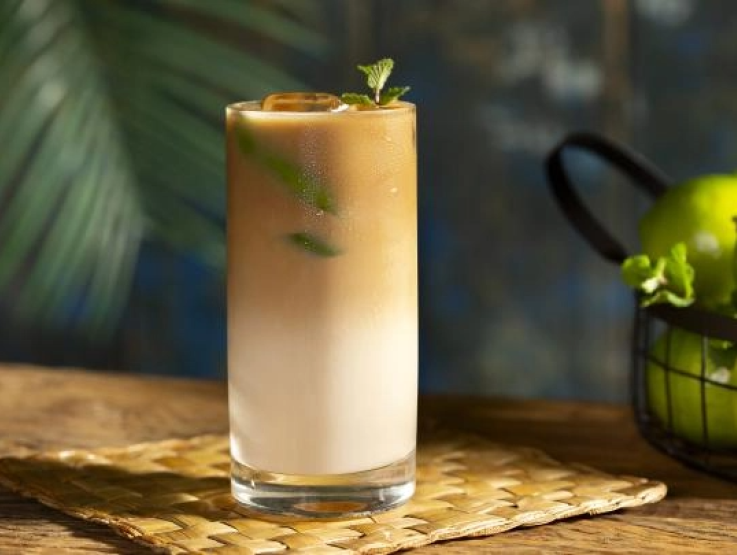 A refreshing glass of iced coffee garnished with lime slices and fresh mint leaves.
