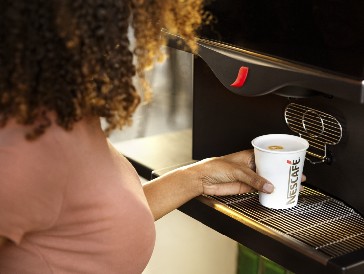 A woman holding a cup of coffee she just poured from a coffee machine.