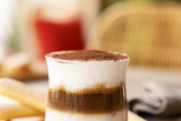 A dessert in a clear glass, featuring vibrant layers, rests on a rustic wooden tray.