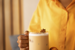 A person enjoys a glass of coffee garnished with cinnamon sticks.