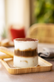 A dessert in a clear glass, featuring vibrant layers, rests on a rustic wooden tray.