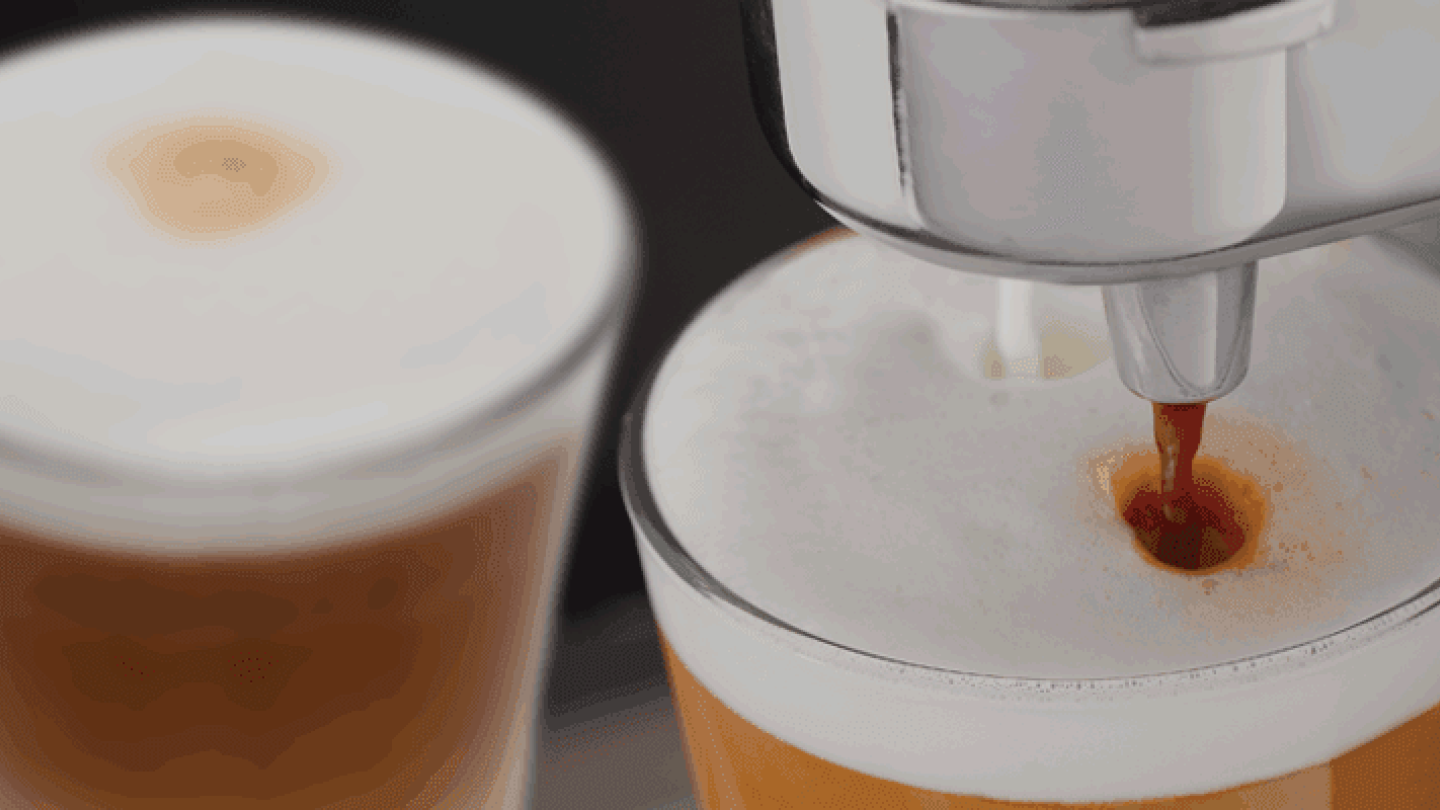 A coffee machine pours fresh coffee into a clear glass, creating a warm and inviting scene.