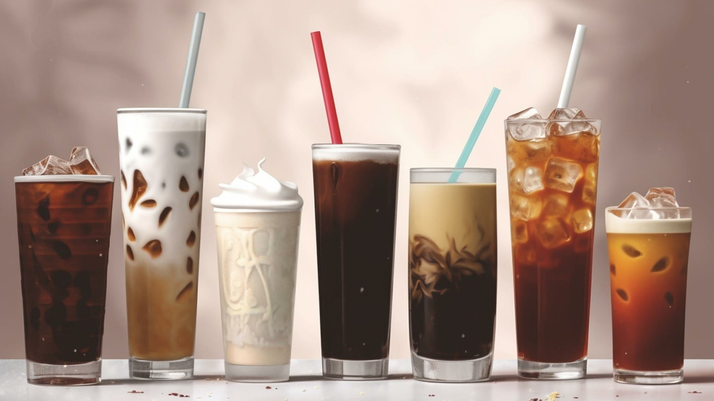 A variety of iced drinks in colorful glasses, including iced coffee, tea, and fruit smoothies on a wooden table.