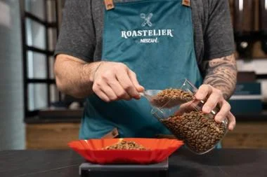 A man in an apron pours coffee from a pot into a bowl.