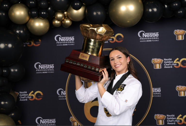 Chef Emily Morgan in uniform proudly holds a trophy, celebrating her trio of gold medals for a winning three-course menu.